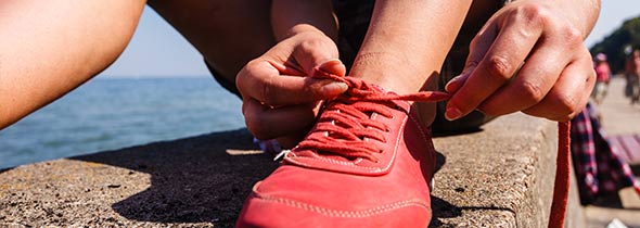 Une femme lace ses chaussures de sport rouge. On voit la mer.